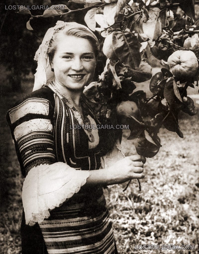 Младо момиче в народна носия позира до овощно дърво, 30-те години на ХХ век
