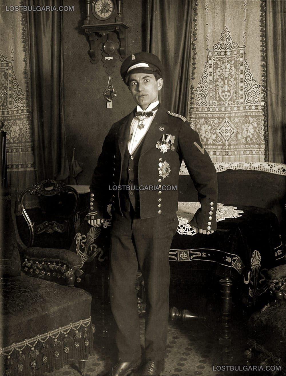 Млад мъж, облечен в бутафорна униформа, на фона на интериор от началото на ХХ век