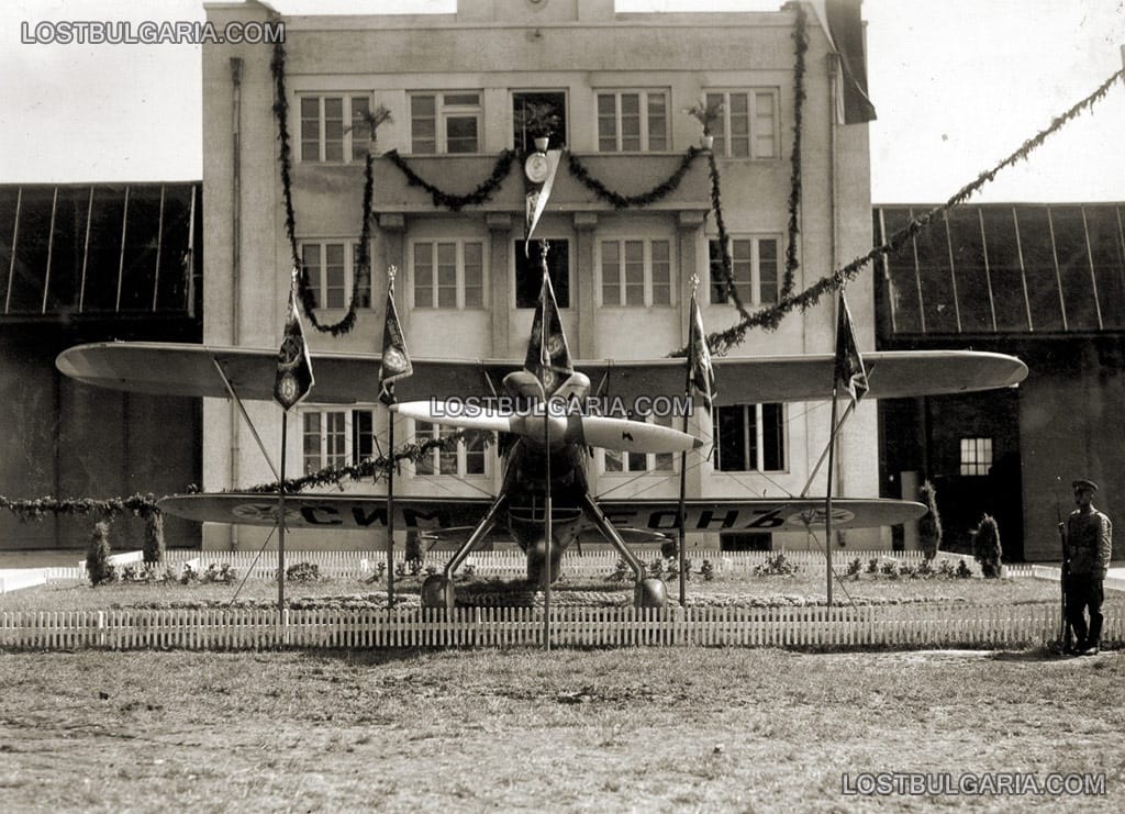 Изтребител Heinkel He 51B "Сокол" на 26 юни 1937 г. на летище Божурище, ограден с бойните знамена на авиационните полкове на възраждащата се българска военна авиация