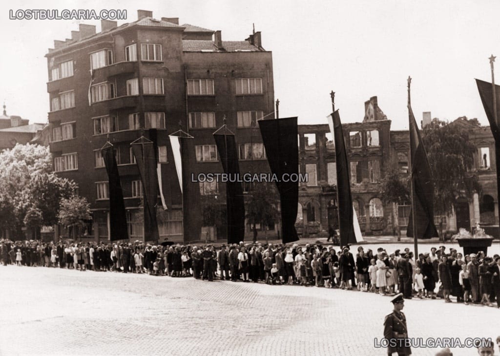 Опашка от чакащи за поклонение пред тялото на Георги Димитров на фона на бомбардирани сгради на пл. "Народно събрание", София, юли 1949 г.