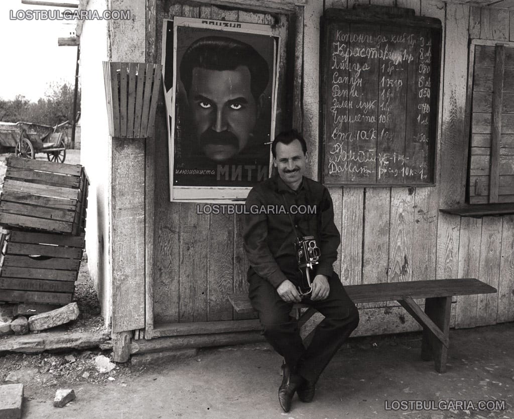 Мъж с фотоапарат седи пред селски магазин с плакат на факира Мити, 50-те години на ХХ век