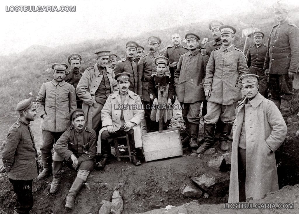 Български войници и офицери, и дете с униформа, осиновено от полка, с останки от 18-килограмов снаряд на 58-милиметрова френска минохвъргачка, фронта в Македония, 12 февруари 1917 година