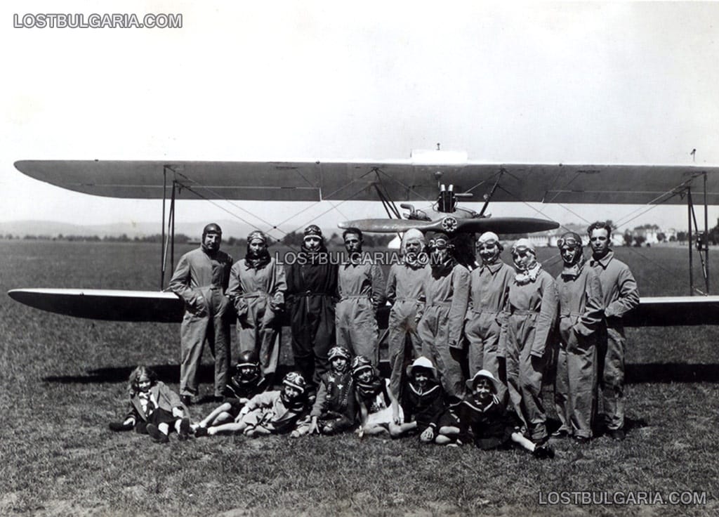 Пилоти с децата и жените си, облечени с летателни костюми, позират пред биплан, края на 20-те години на ХХ век
