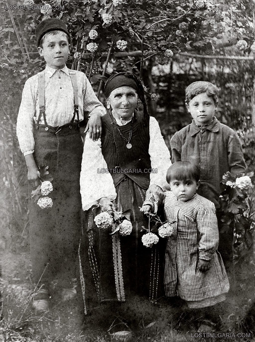 Възрастна жена, облечена в носия, със своите внуци, село Лъжане, Орханийско (Трудовец, Ботевградско), около 1923 г.