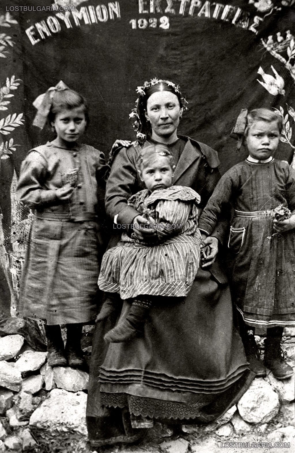 Млада жена с три деца пред знаме с надпис на гръцки "Спомен кампания" (ΕΝΘΥΜΙΟΝ ΕΚΣΤΡΑΤΕΙΑΣ), 1922 г., вероятно Пазарджик