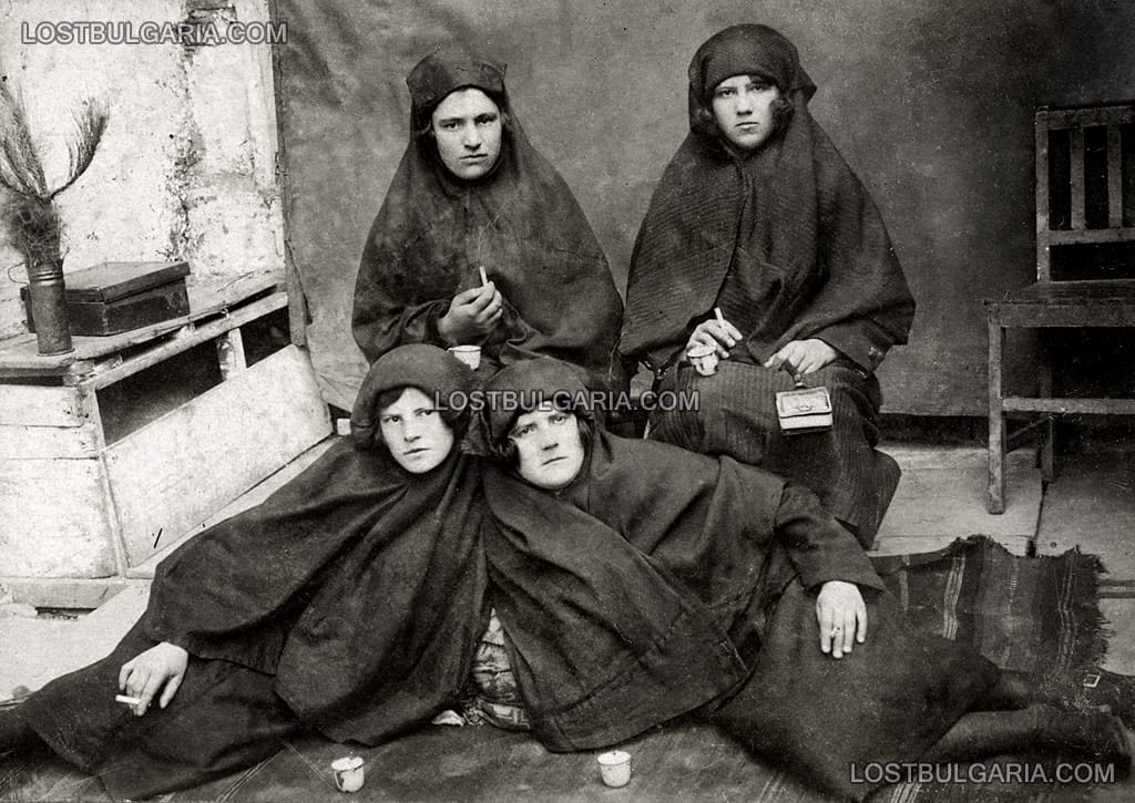 Четири момичета, облечени в странни одежди, позират държейки цигари, неизвестно къде, вероятно началото на 20-те години на ХХ век