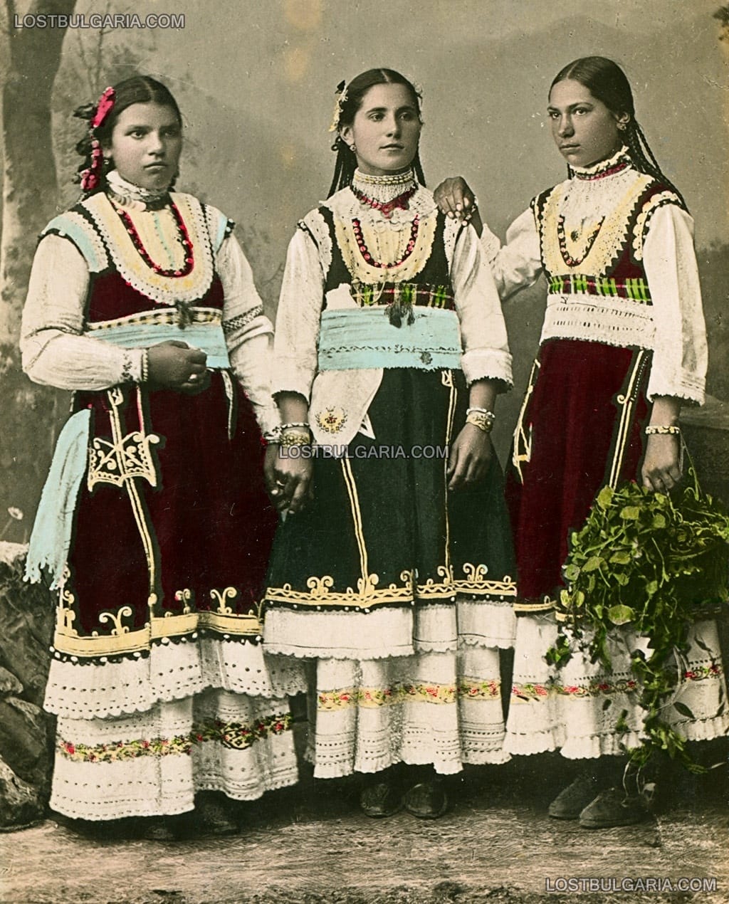 Оцветена фотография на три млади момичета, облечени в носии от Софийско, началото на ХХ век