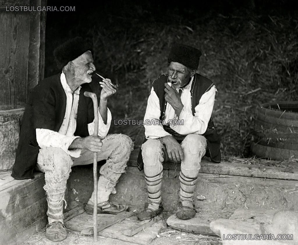 Възрастни мъже, облечени в шопски носии пушат лули и разговарят, 20-те години на ХХ век