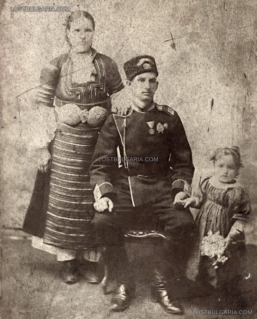 Семейна фотография на участник в Сръбско-Българската война, награден с медал за участие във войната и знаци за отлична и за първоразрядна стрелба, заснет в София след 1885 г.