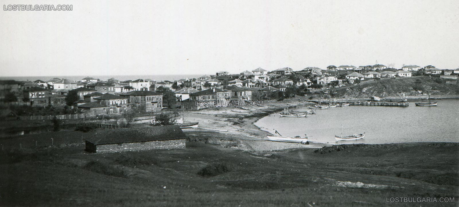 Панорамен изглед към Ахтопол с пристанището и аламаните на рибарската кооперация, вдясно в близост до кея се виждат и останките от крепостната стена, вероятно 30-те години на ХХ век
